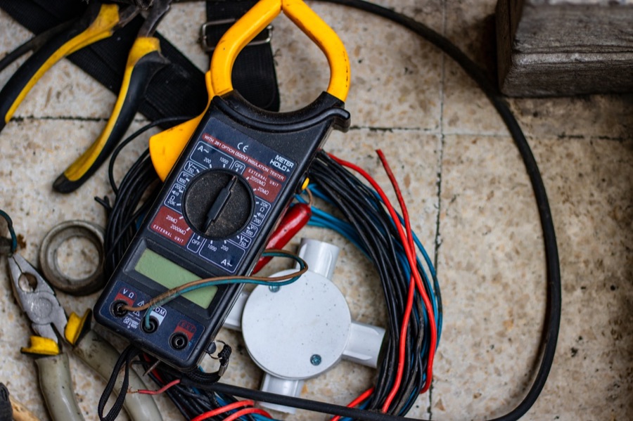 Alicate amperímetro pousado entre fios elétricos e alicates