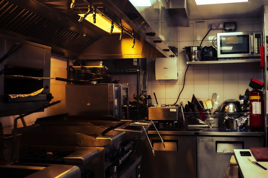 Cozinha profissional de restaurante com hotte de exaustão em aço inox sobre a linha de fogões e fritadeiras