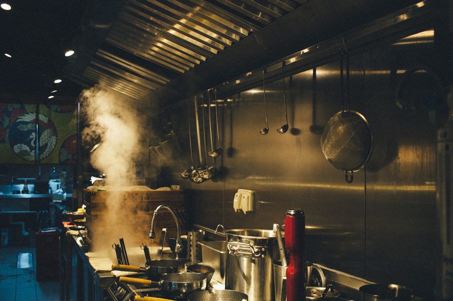 Hotte de exaustão em aço inox sobre a bancada de cozedura de um restaurante, com vapor a subir para o canal de extração