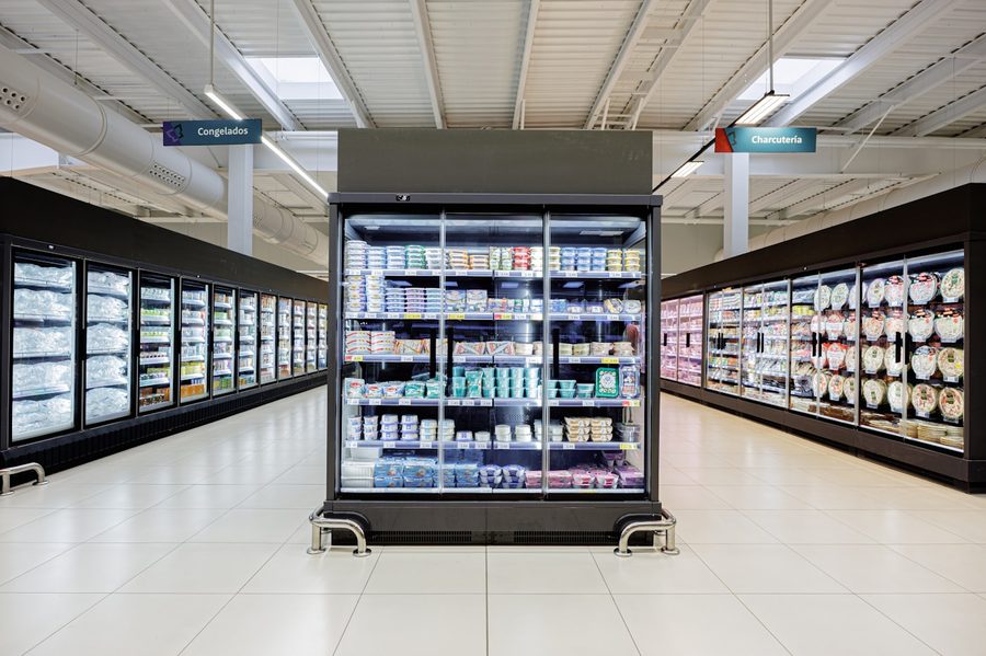 Corredor de supermercado com murais frigoríficos de portas de vidro dos dois lados e um expositor de congelação ao centro