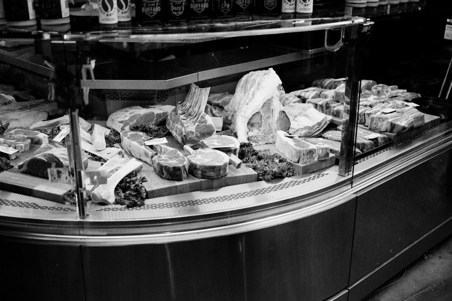 Vitrina de talho com tampo de vidro curvo e vários cortes de carne expostos sobre tábuas de madeira