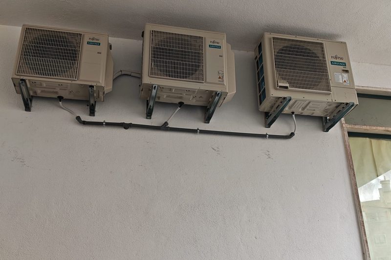 Três unidades exteriores Fujitsu Airstage instaladas em fila sob um beiral