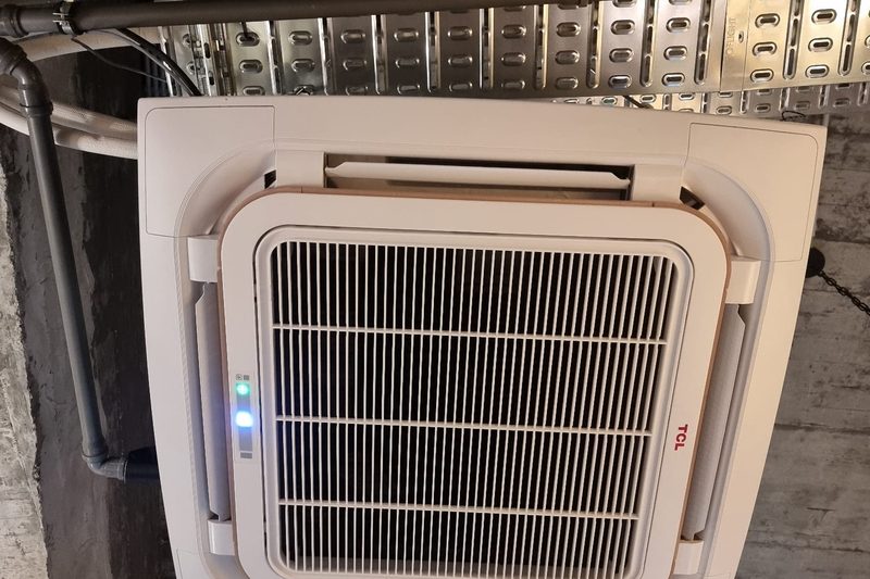 Cassete de teto instalada num tecto técnico em betão, com calhas elétricas visíveis