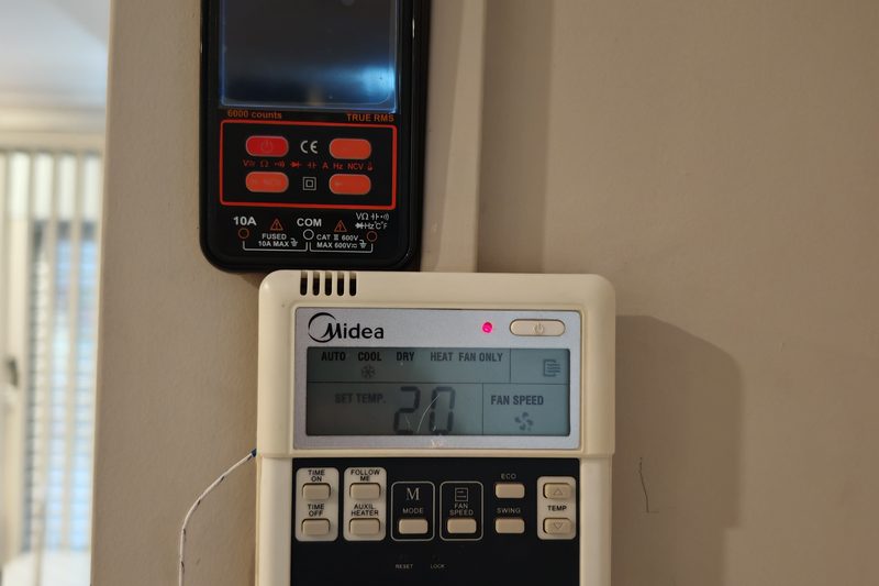 Medição elétrica com multímetro junto a um comando de parede Midea
